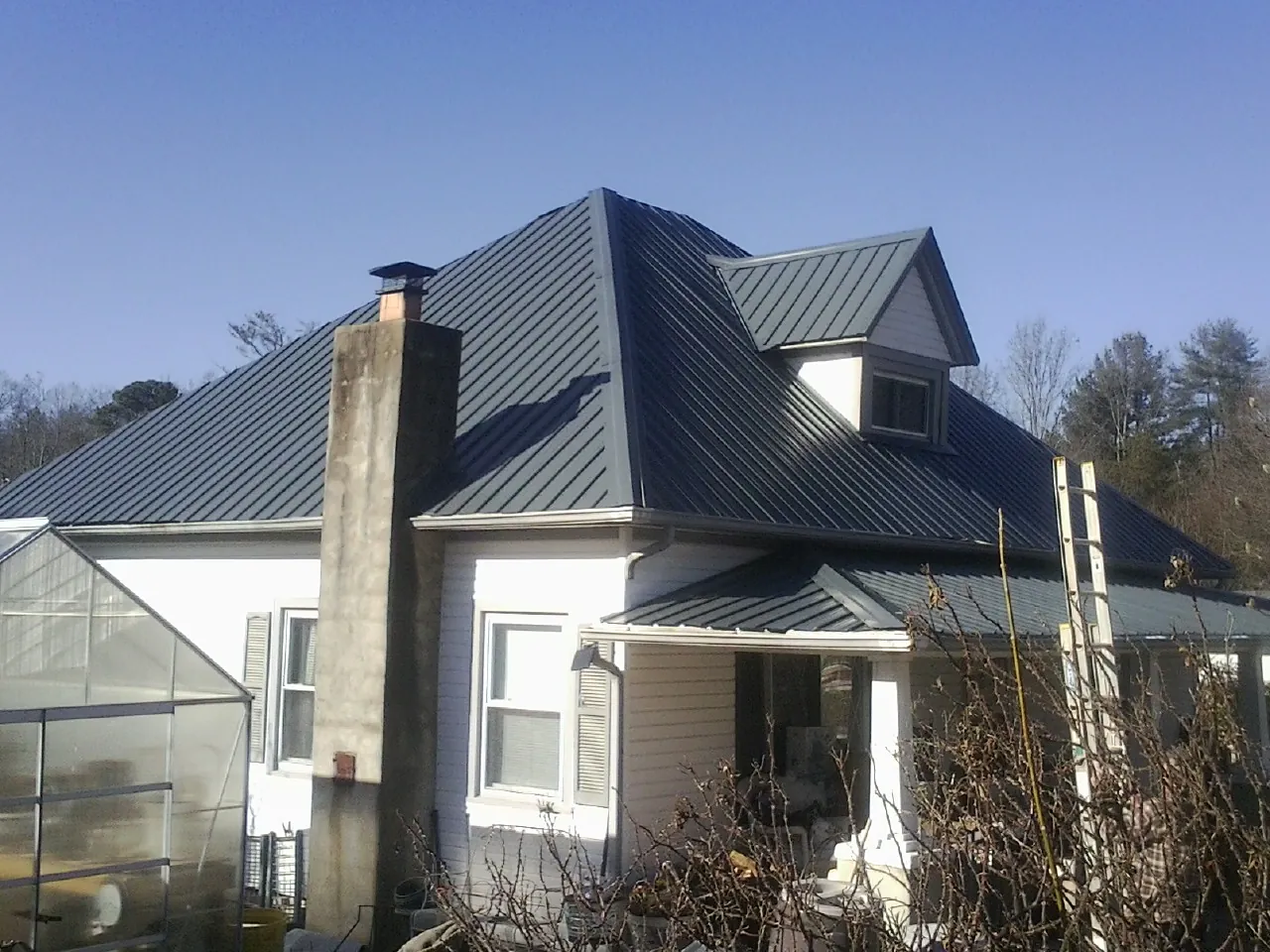 Dark blue standing seam metal roof on a white farmhouse with dormer — Slate & Tile Roof Repair by Roofing Brothers in Sperry