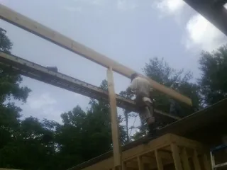 Carpenter setting a ridge beam over a new addition frame in Sperry