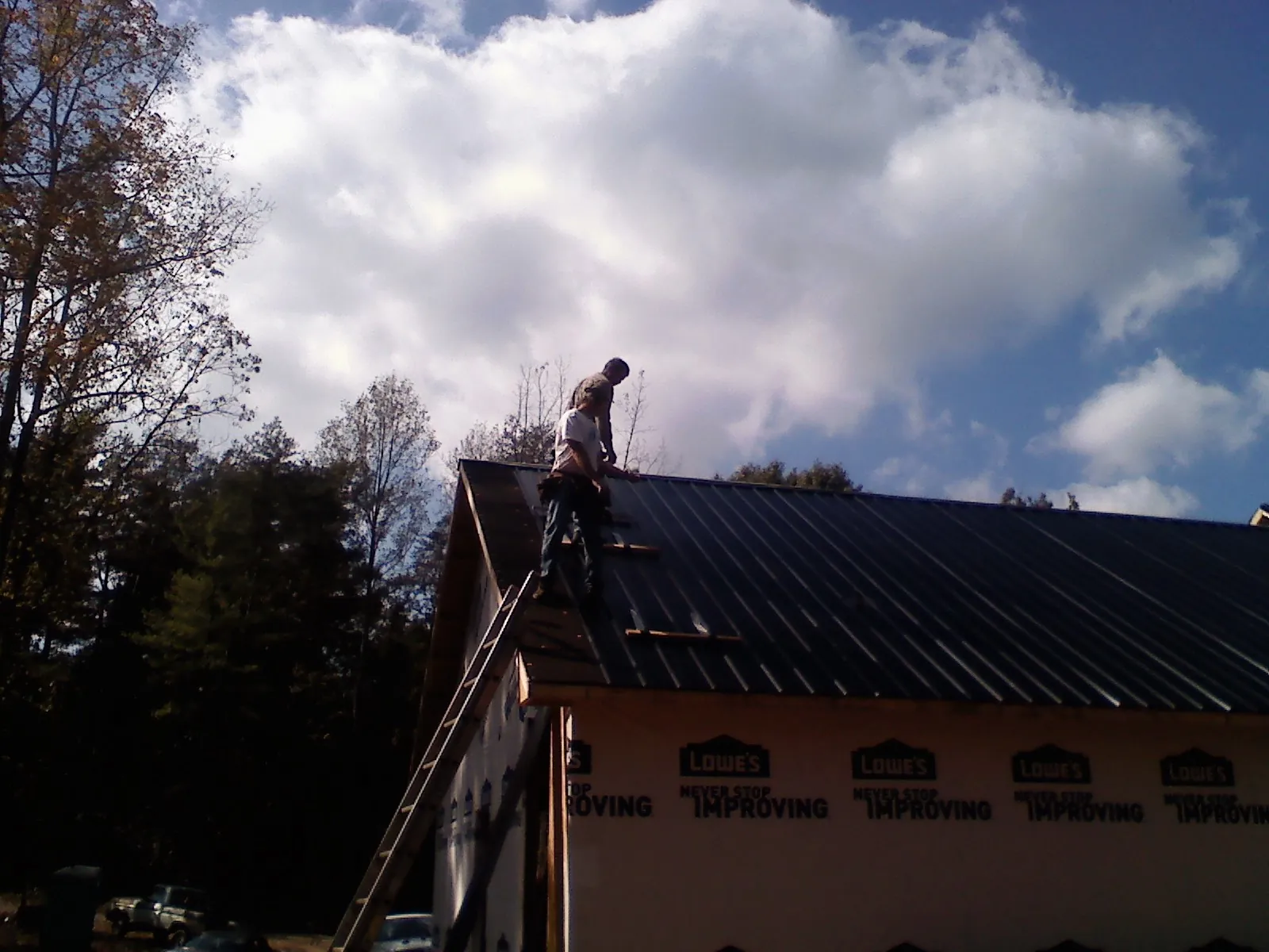 Roofer fastening dark metal panels high against a cloudy sky, from a Roof Inspection job in Sperry